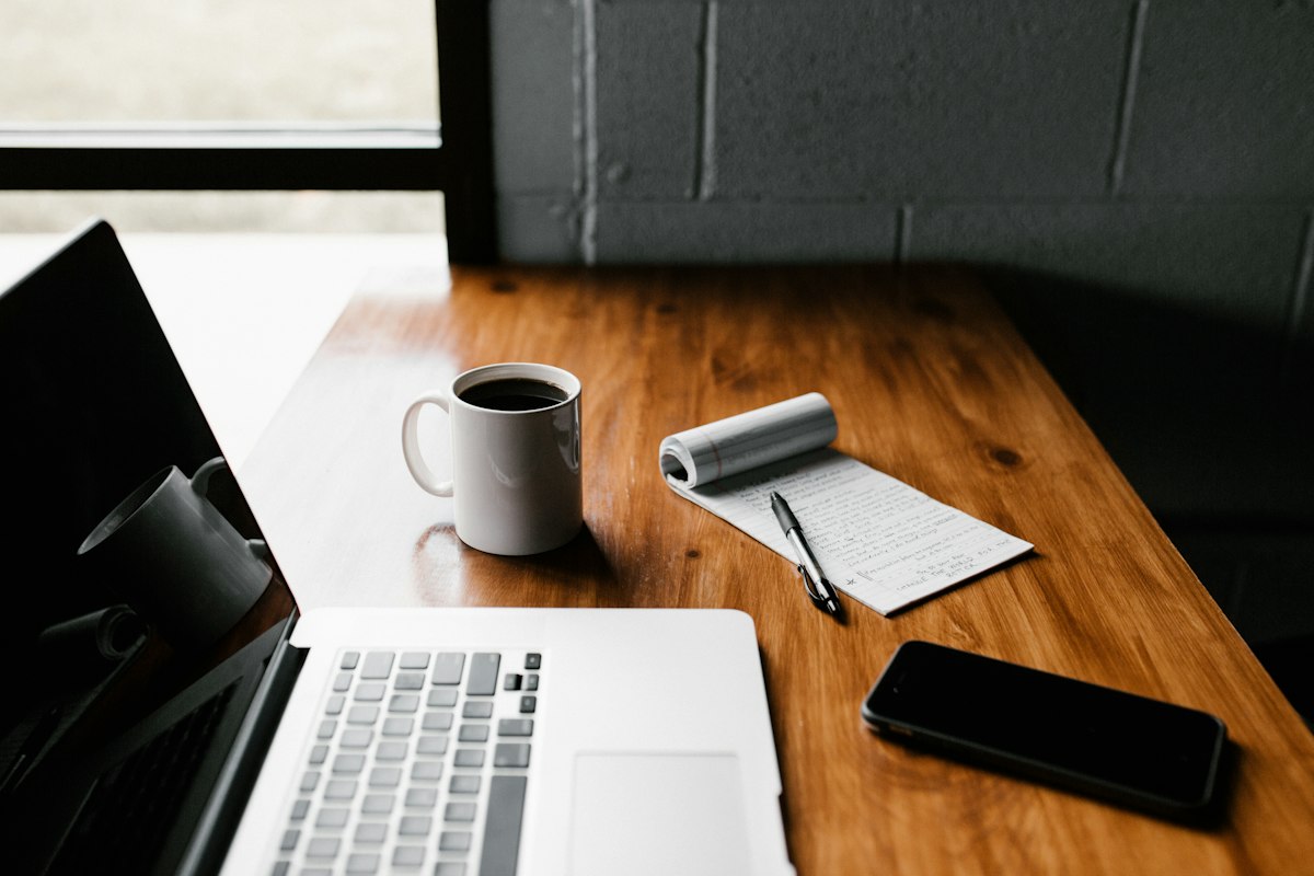 Laptop with a notebook and coffee on a work desk